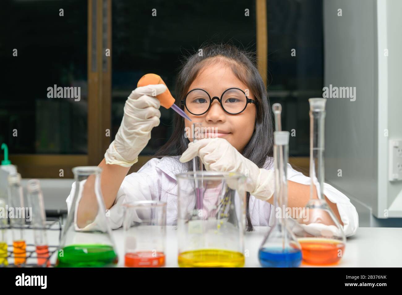 Happy little girl wearing lab coat making experiment in chemical