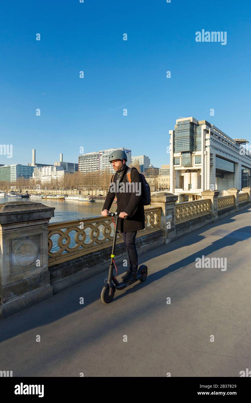France, Paris, riverbanks of the Seine river listed as World Heritage by UNESCO, building hosting the Ministry of Finances and Economy by architects Paul Chemetov and Borja Huidobro and the business district around Gare de Lyon (Lyon train station), man on a scooter on Bercy bridge Stock Photo