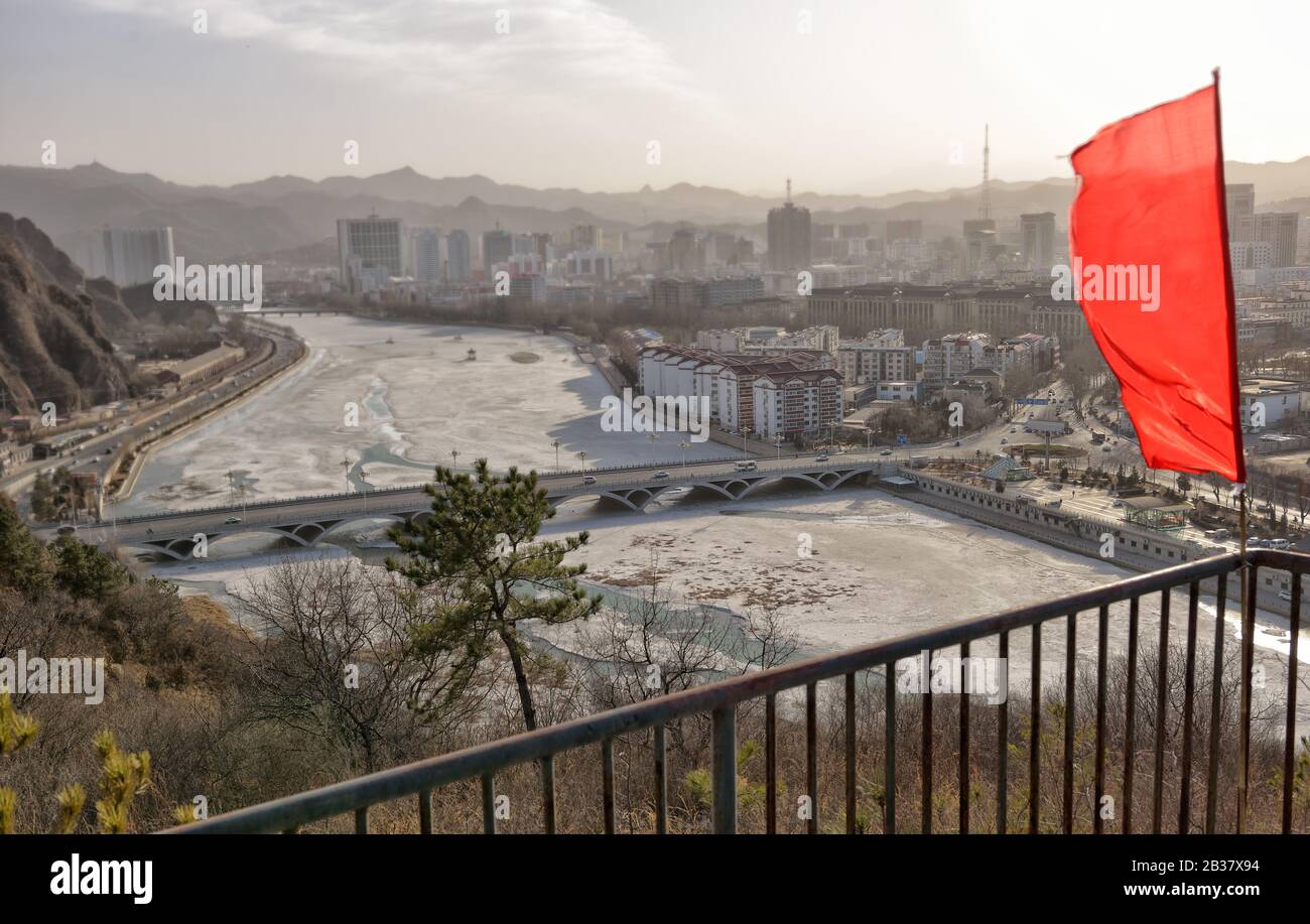 Red flag moving inn the wind over Chengde city. Aerial view of the bridge, frozen river and downtown, Hebei province (China), in winter. Stock Photo