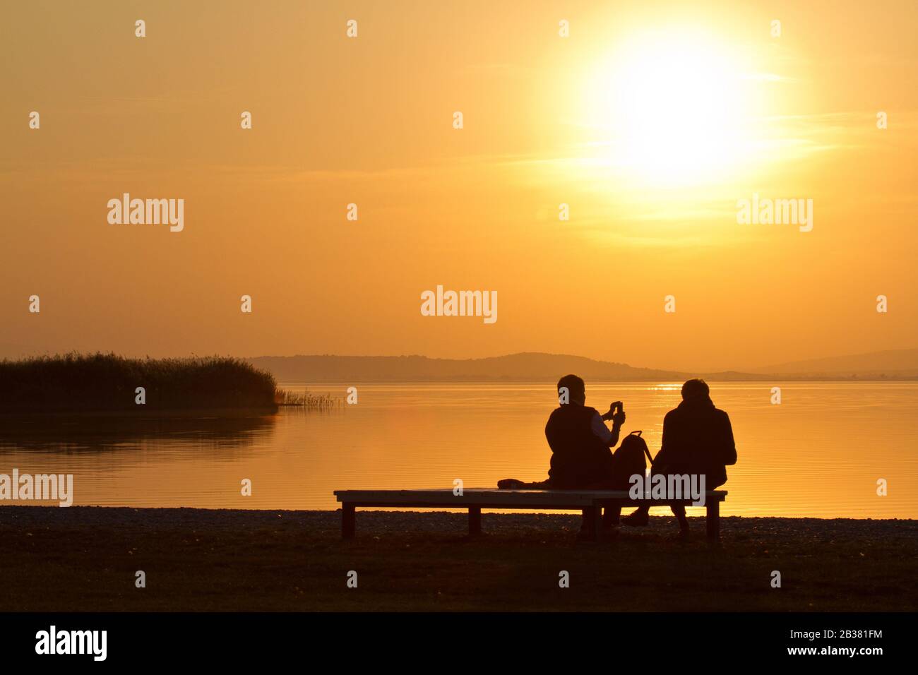 Abendstimmung am Neusiedler See, Paar auf Parkbank schaut auf den See, Silhouette, Stock Photo