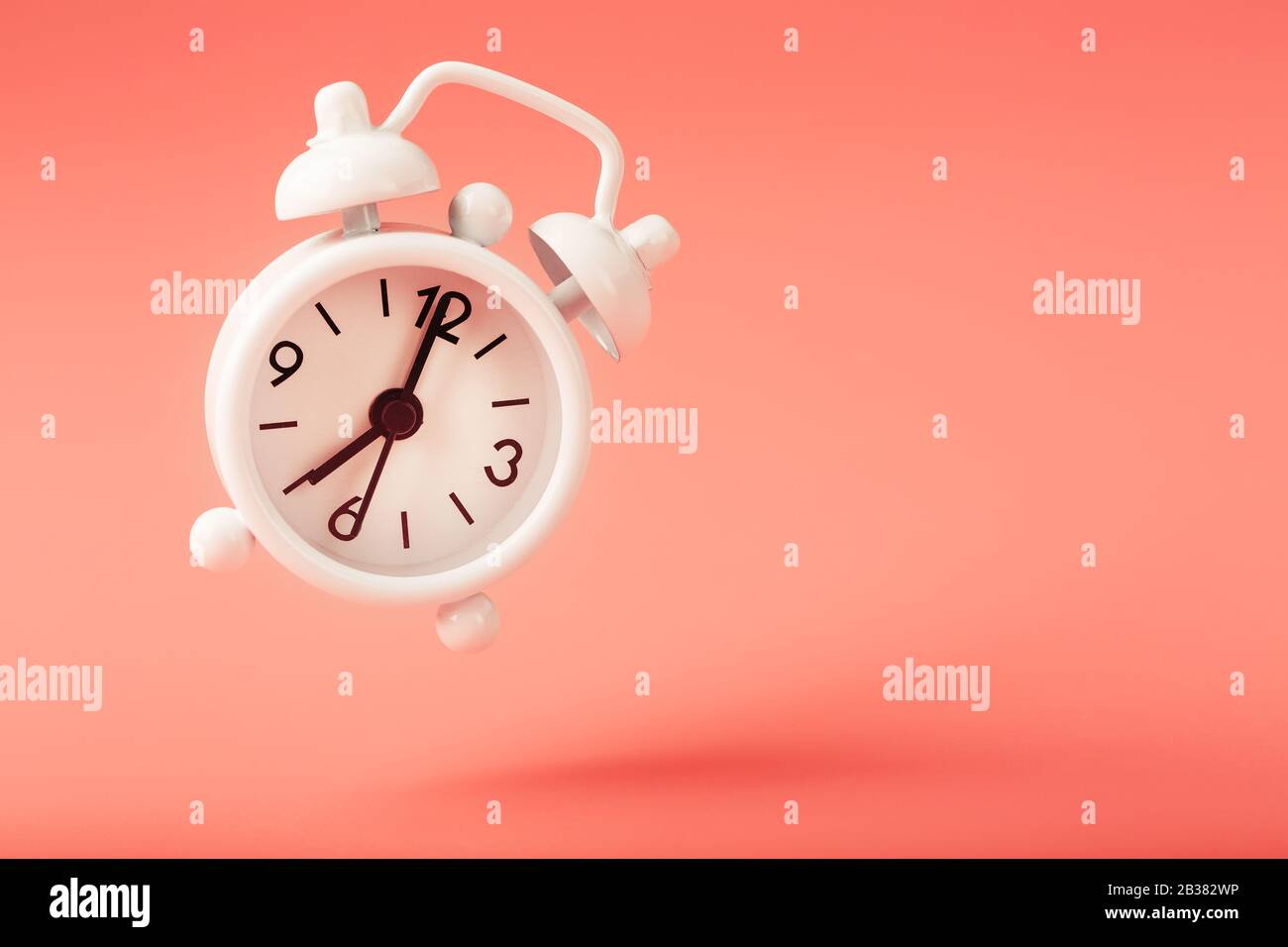 White alarm clock in levitation with shadow isolated on pink background. Hands on the clock 7. Minimalistic creative modern still life concept Stock Photo