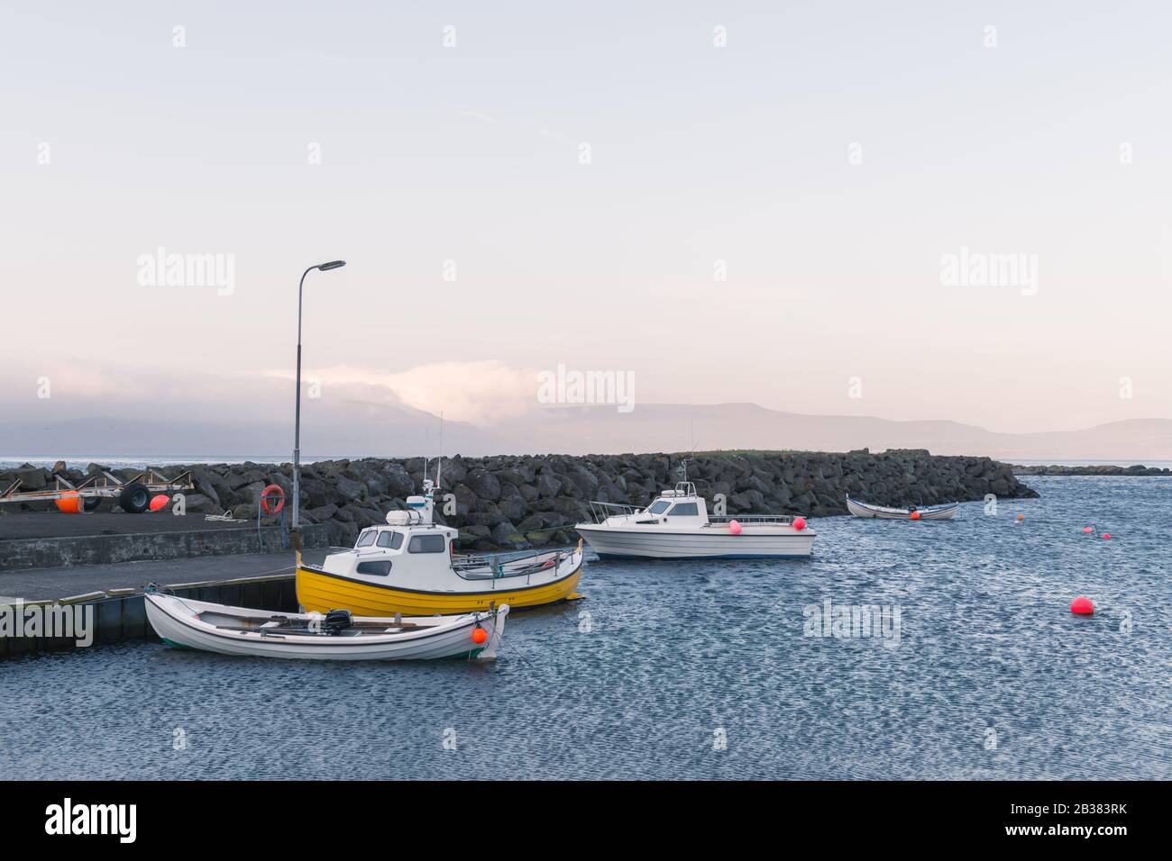 Foggy morning view of a boats docking in a small pier of Kirkjubour village on Streymoy island, Faroe islands, Denmark Stock Photo