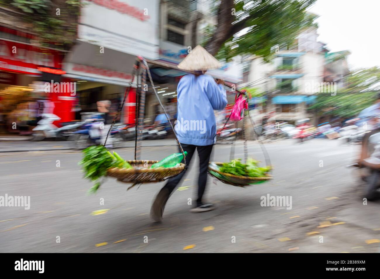 Motion blurred photograph of local Vietnamese woman selling vegetables from baskets on the streets of Hanoi, Vietnam, South East Asia Stock Photo