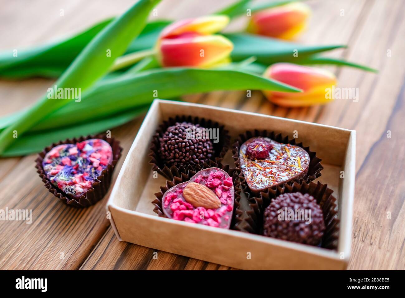 Handmade sweets in a box next to tulips for the holiday, wooden background. On march 8 Stock Photo