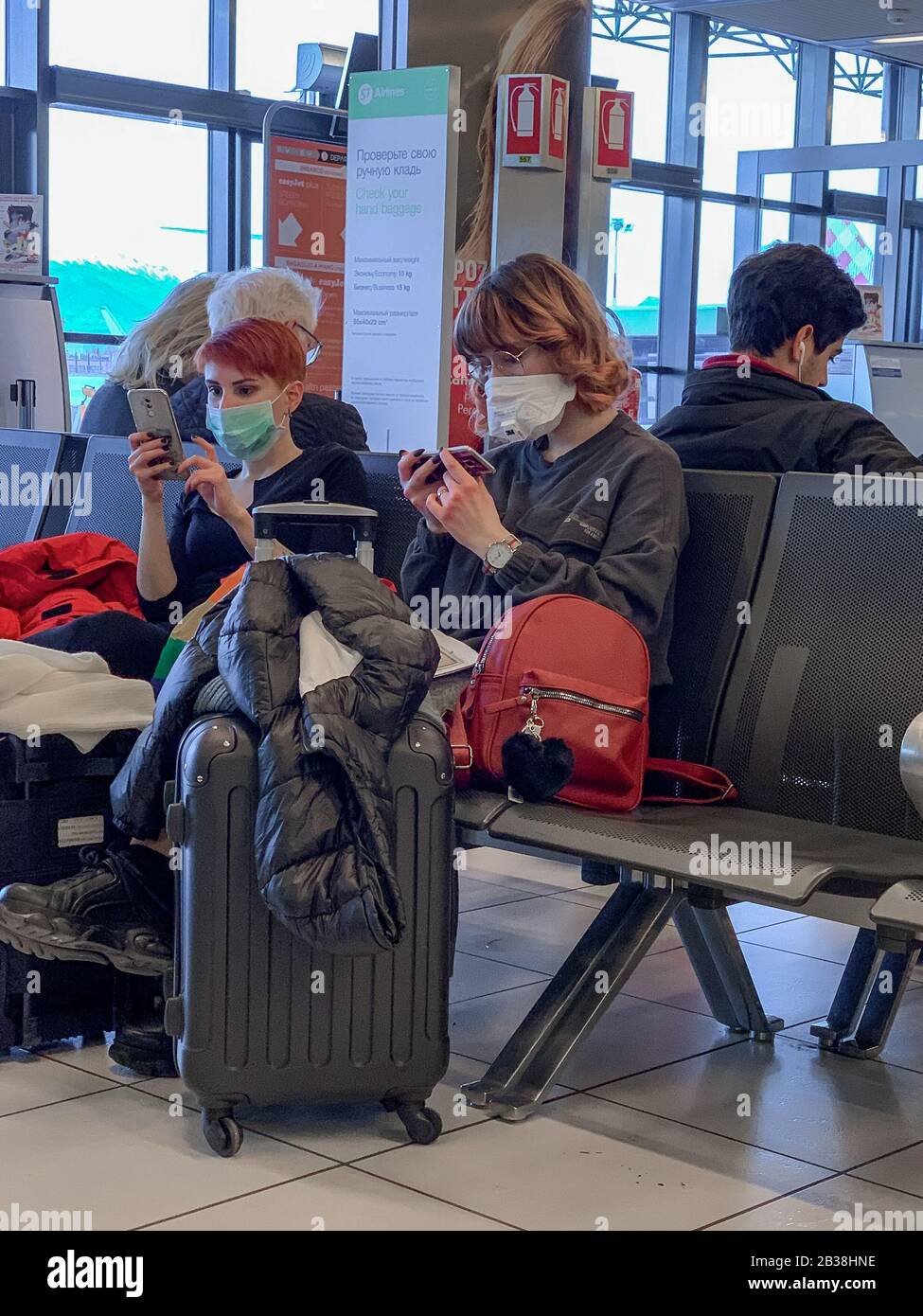 Villafranca Catullo Airport, Italy - February 27th 2020: two young italian girls wearing protective masks at the airport gate while they use their pho Stock Photo
