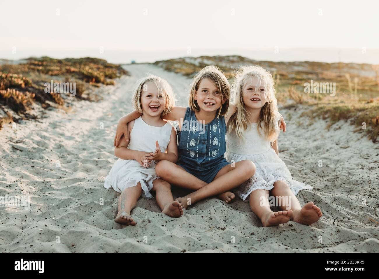 Portrait of three young sisters embracing and smiling in sand Stock Photo