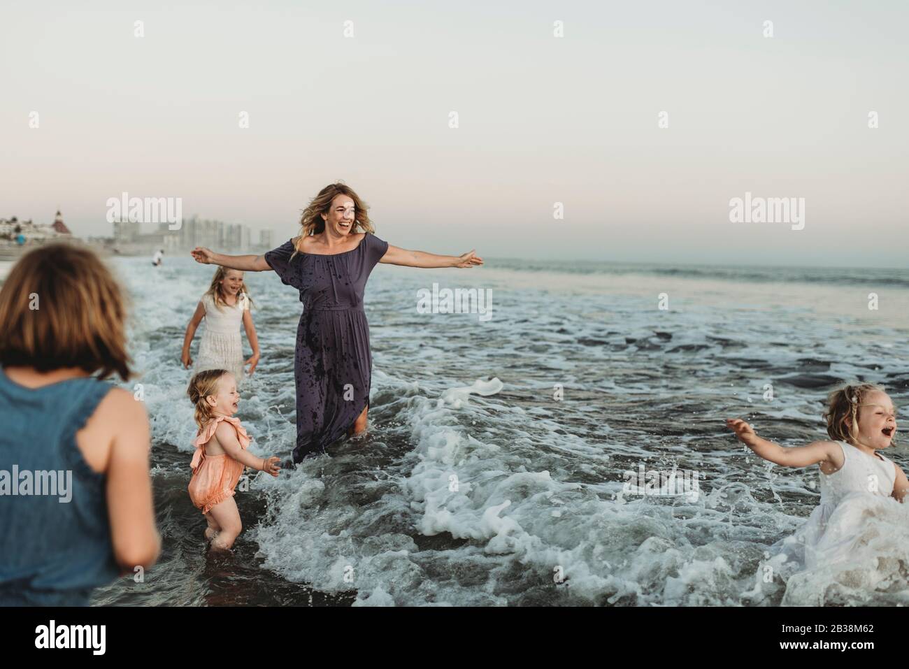 Strong mother with four daughters playing in ocean at sunset Stock Photo