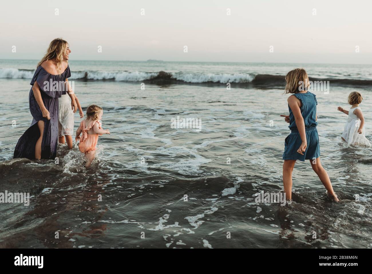 Strong mother with four daughters playing in ocean at sunset Stock Photo