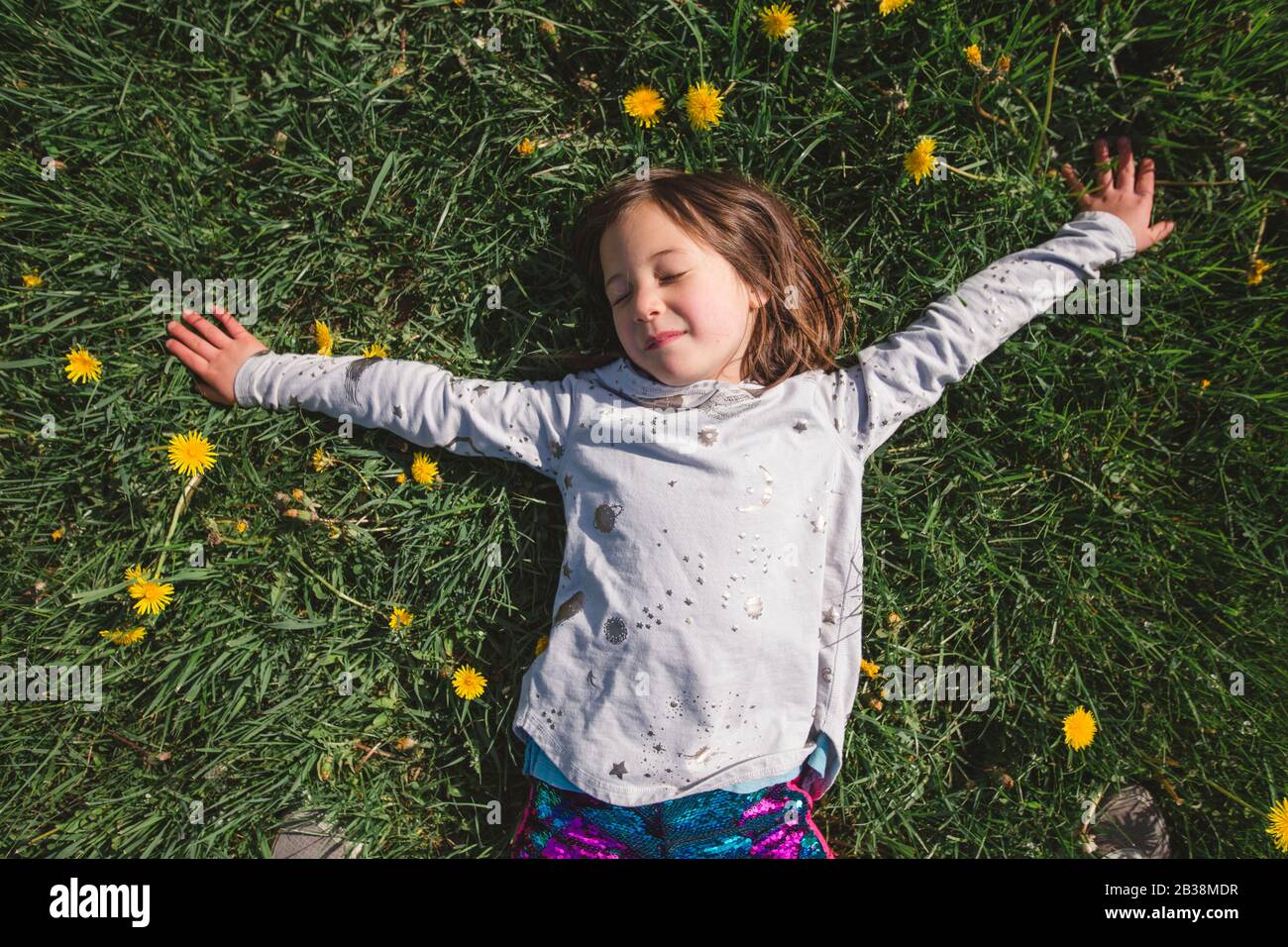 A happy child lays down in a field of wildflowers with closed eyes Stock Photo