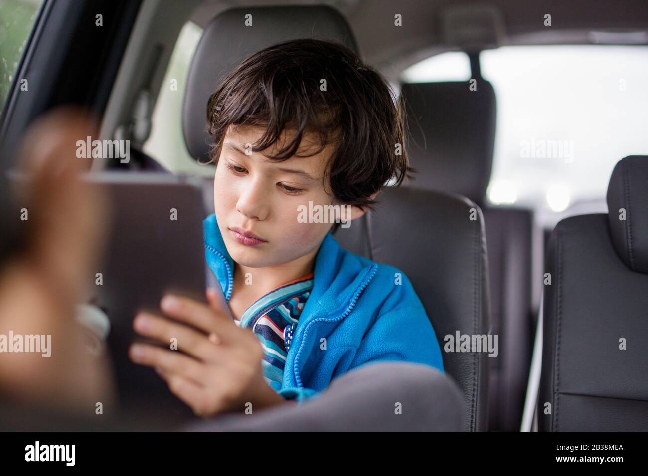 A boy sits in a carseat on a car trip watching a tablet Stock Photo
