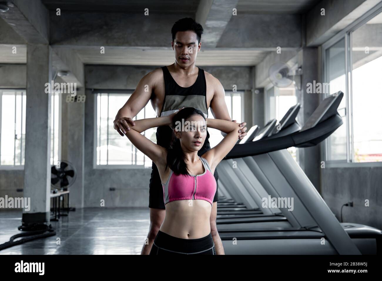 Asian sexy women stretch before exercising on yoga mat with trainer man in the gym. Concept of exercise in gym. Handsome man stretch to beautiful woma Stock Photo
