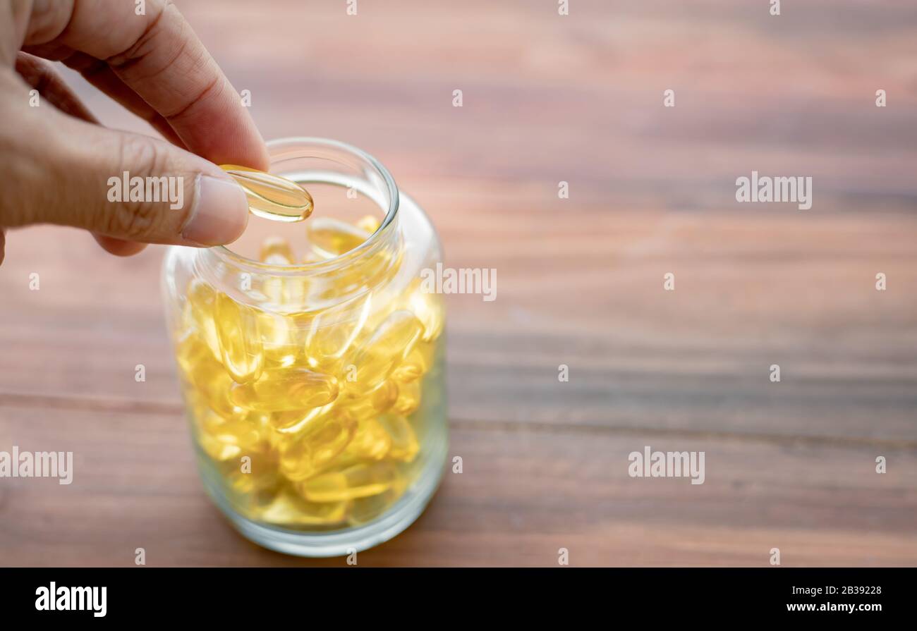 Closeup hand picked medicine, supplements from glass bottles on a wooden background for eating. Gold fish oil capsules. Concept of medicine in medical Stock Photo