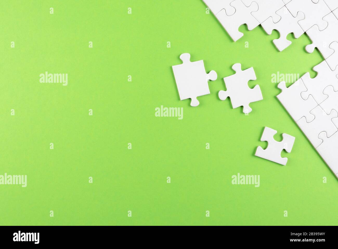 top view of white blank unfinished jigsaw puzzle on green background, completing a task or solving a problem concept Stock Photo