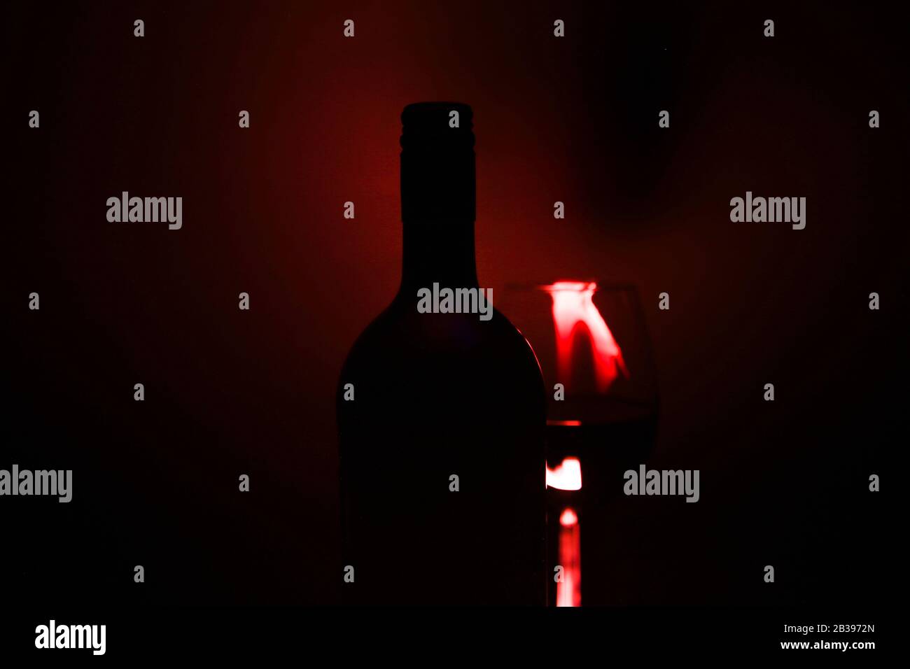 Studio shot of isolated dark black blurred red wine bottle silhouette with glass (focus on bottle neck) Stock Photo