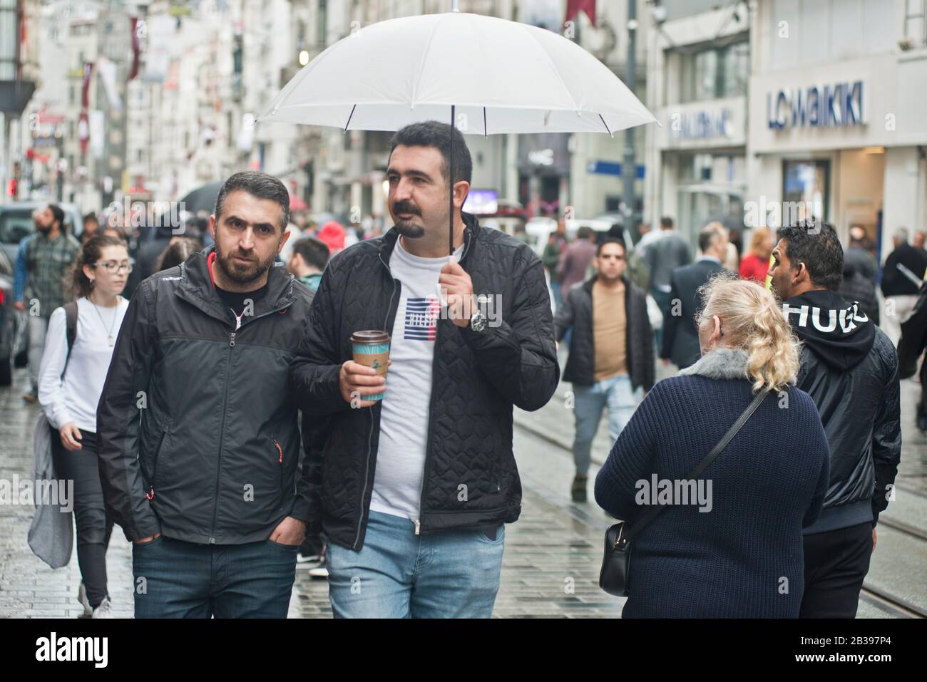 Istanbul: men  walking under the rain with an umbrella in Istiklal avenue. Turkey Stock Photo