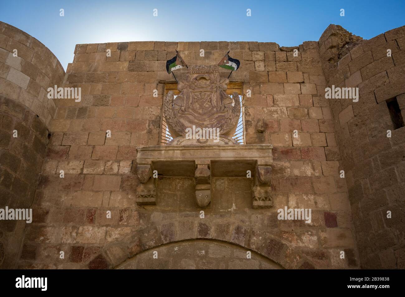 Jordan, Aqaba, street view from the front gate of Aqaba Castle with coat of arms with two Jordanian flags above the main fortress gate. Sunny winter day Stock Photo