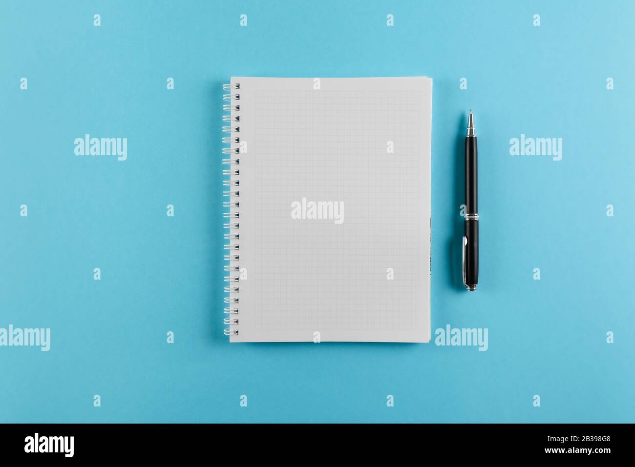 top view of squared spiral notepad and ballpoint pen on blue background Stock Photo