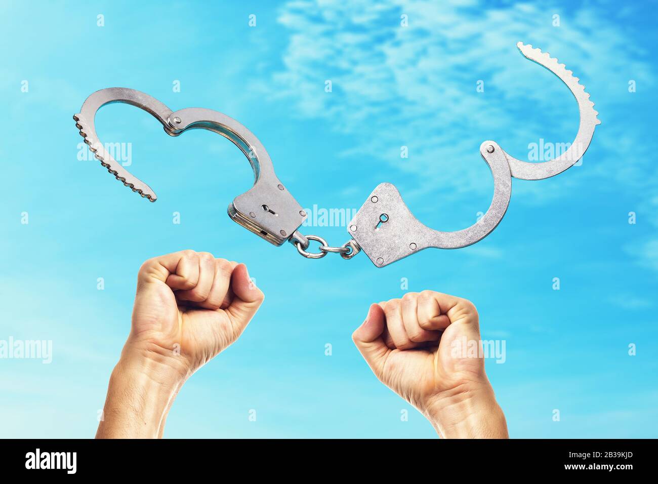 Open handcuffs and hands raised up amid the blue sky. Concept on the price of freedom Stock Photo
