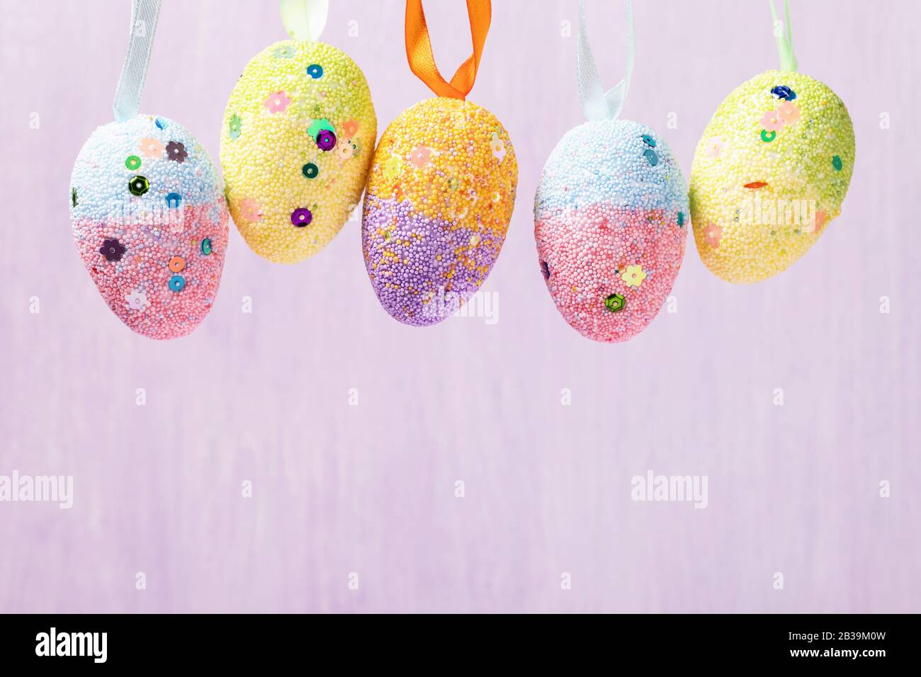 Hanging Easter eggs decorated in various colors. Festive background with copy space Stock Photo