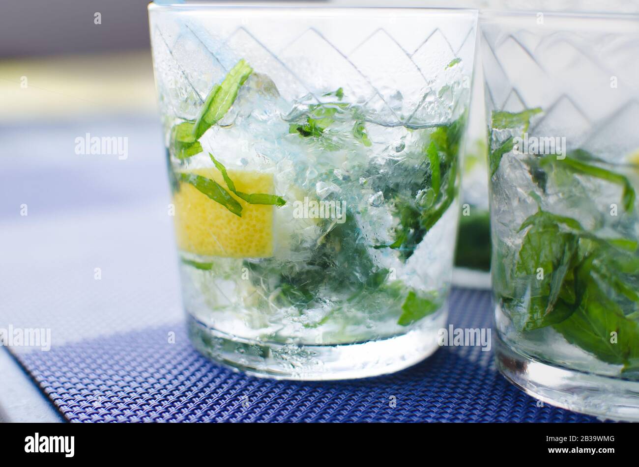full glass of fresh cool transparent water with ice, lemon and , basil leaves on blue table Stock Photo