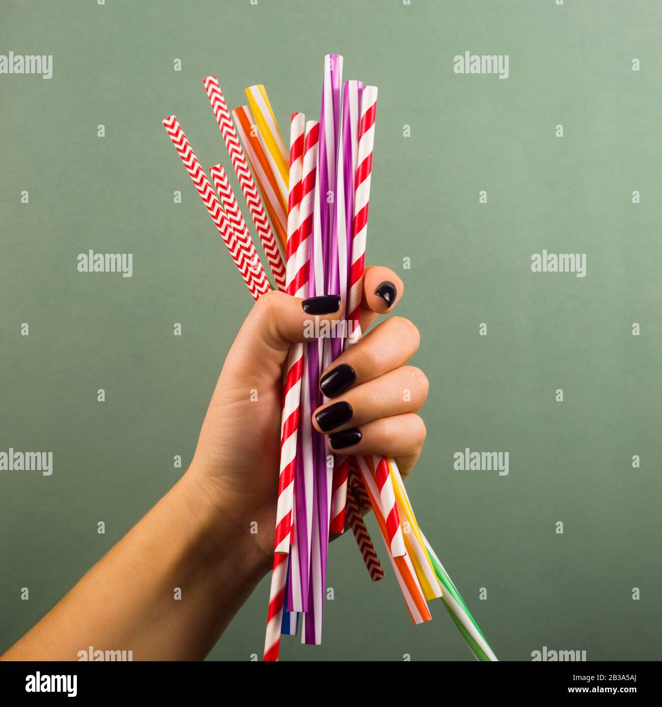 A handful of plastic disposable drinking straws in a female hand on a green background. Not green things, environmental pollution concept. Stock Photo