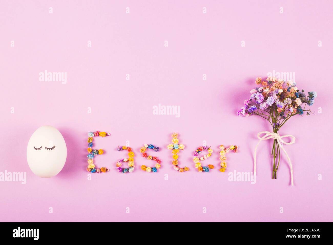 Easter creative layout with the word Easter made of flowers, a bouquet of small flowers and cute eggs on the lilac background. Stock Photo