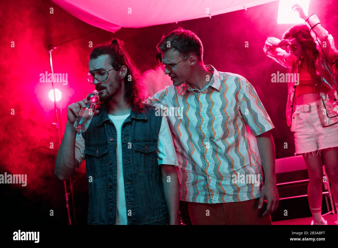 man hugging another man drinking water in nightclub during rave party ...