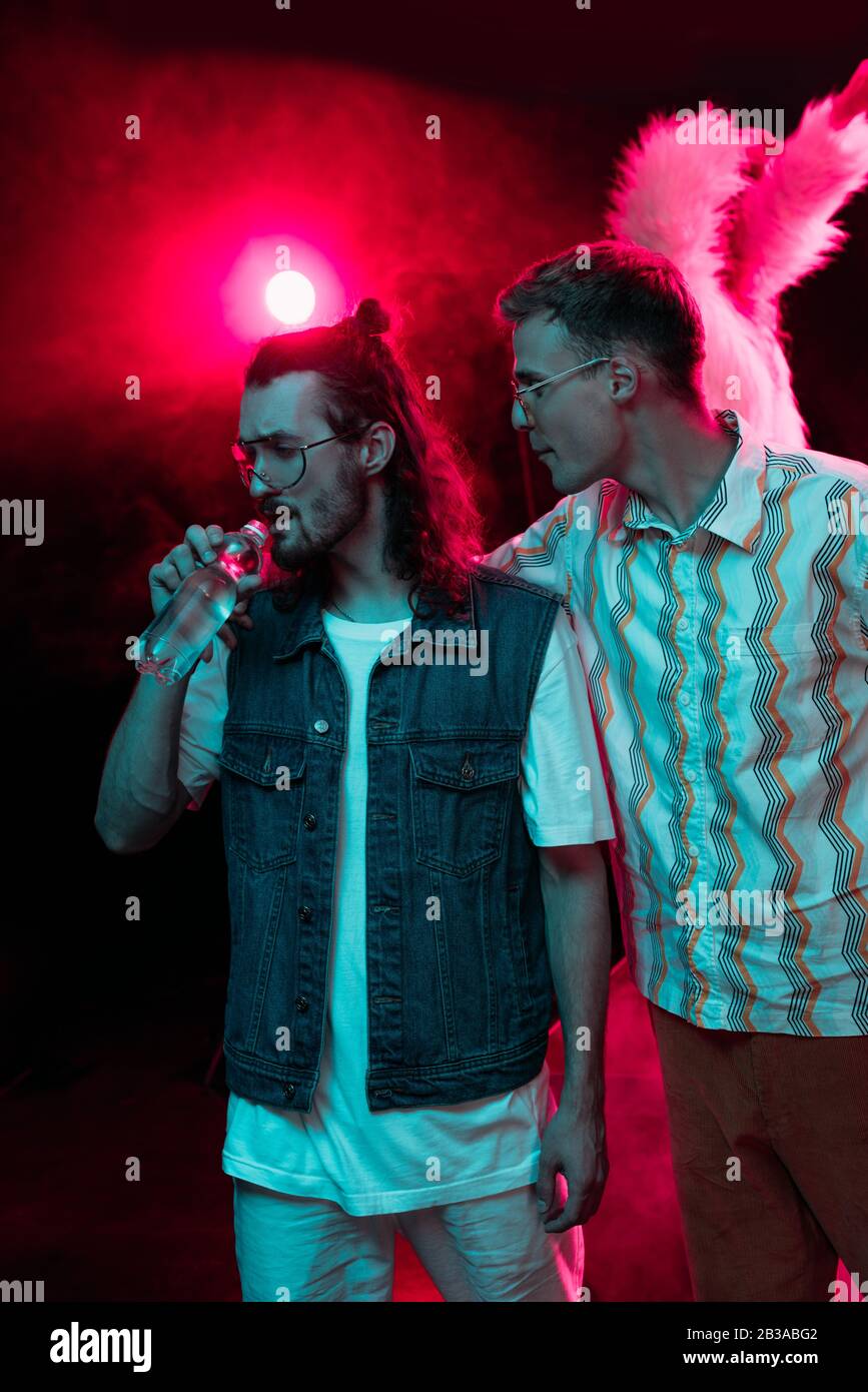 man hugging another man with water bottle in nightclub during rave ...