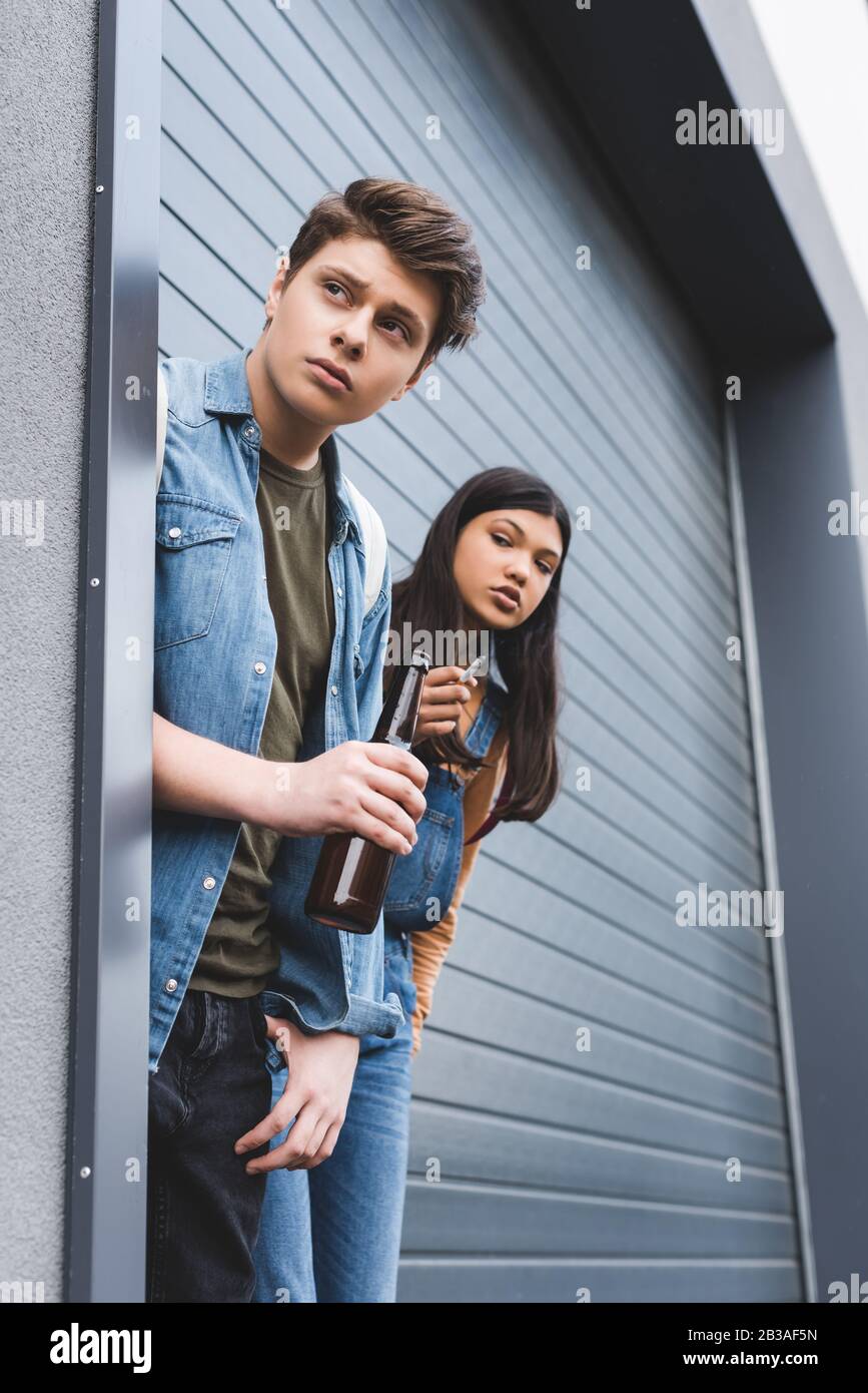 boy and brunette teenager looking away, smoking cigarette and drinking beer Stock Photo