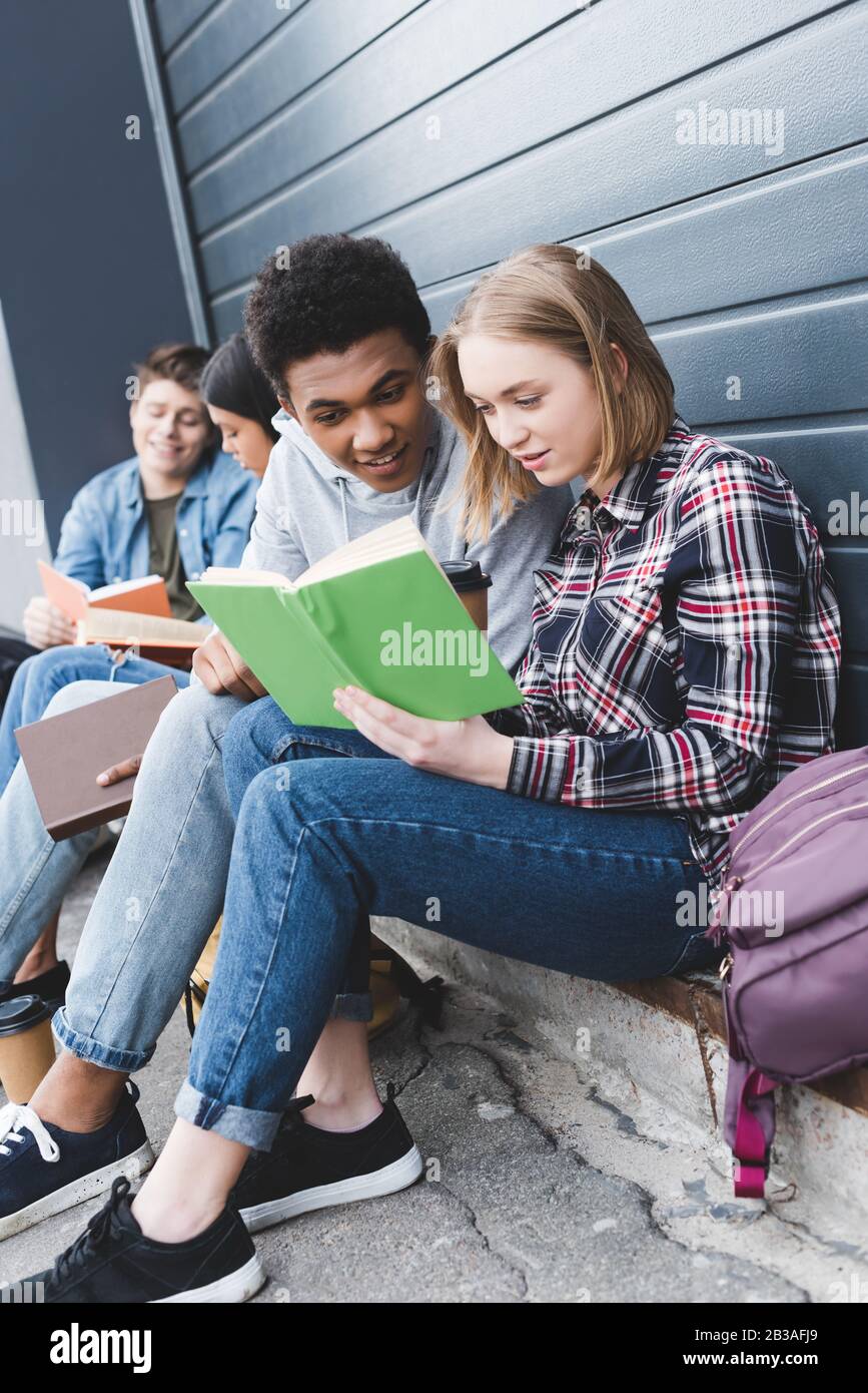 african american and caucasian teenagers sitting, talking and reading ...