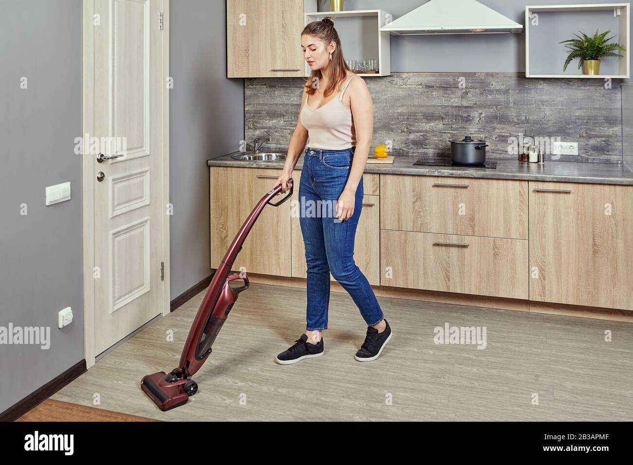 https://c8.alamy.com/comp/2B3APMF/a-young-caucasian-woman-vacuums-a-kitchen-floor-using-a-cordless-vertical-vacuum-cleaner-or-electric-broom-the-maid-is-cleaning-up-the-hostels-cook-2B3APMF.jpg