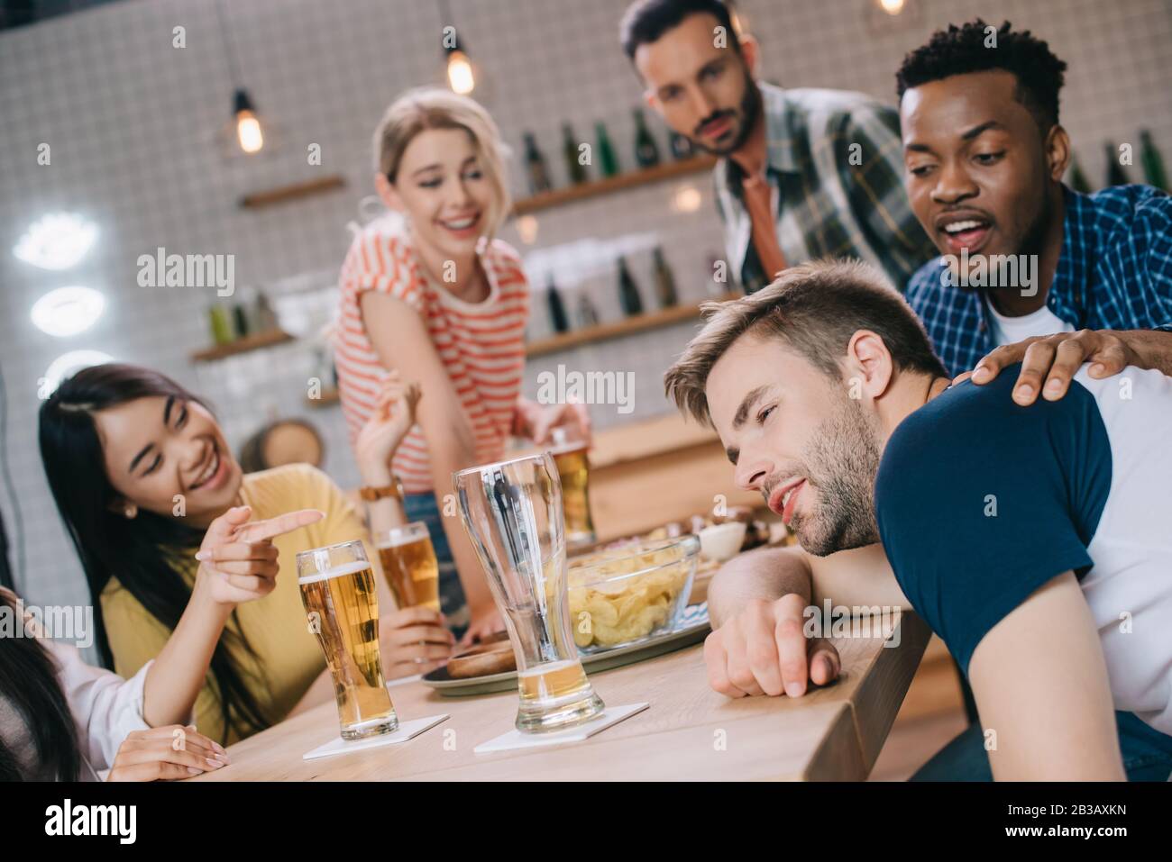 cheerful multicultural friends looking at drunk young man in pub Stock Photo