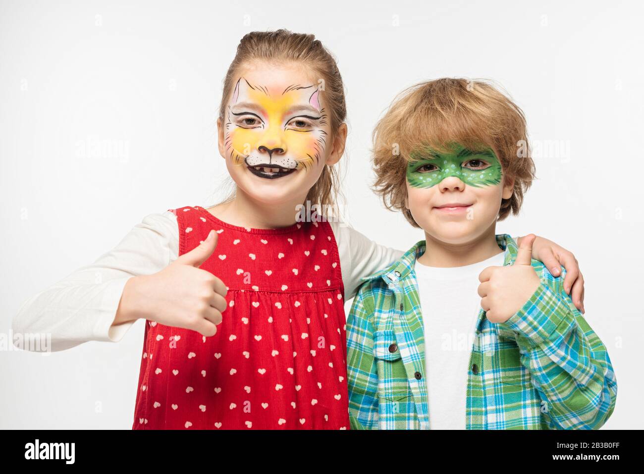 cheerful friends with cat muzzle and gecko mask paintings on faces showing thumbs up isolated on white Stock Photo