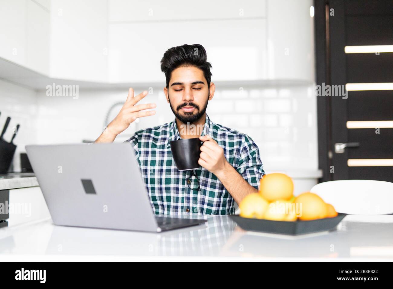 Businessman using a laptop while drinking coffee in his kitchen Stock Photo
