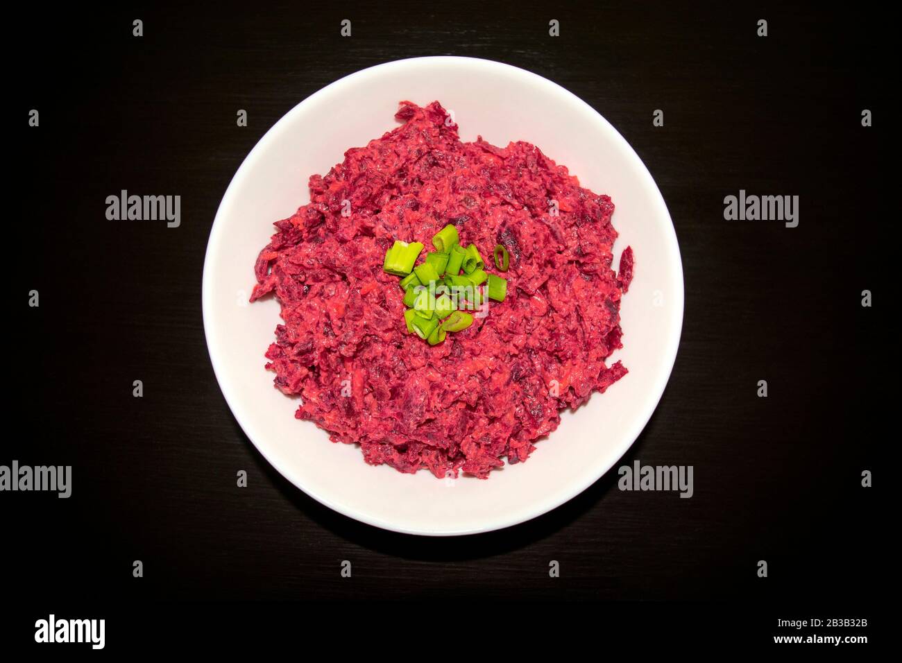 Tasty beet salad in a white bowl on a dark wooden table. Beetroot with cheese, sour cream, and green onion, healthy and fresh food. Stock Photo