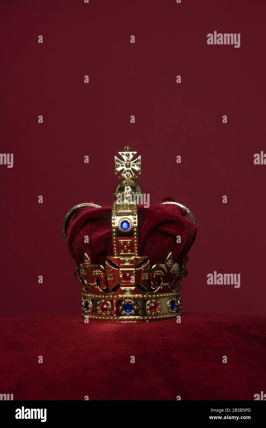 Golden crown on a velvet cushion on a deep red background with copy ...