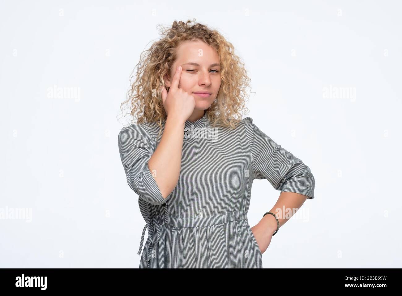 Young caucasian curly woman is touching her eye to show that she has problem with eyesight. Health trouble. Miopia or astigmatism Stock Photo