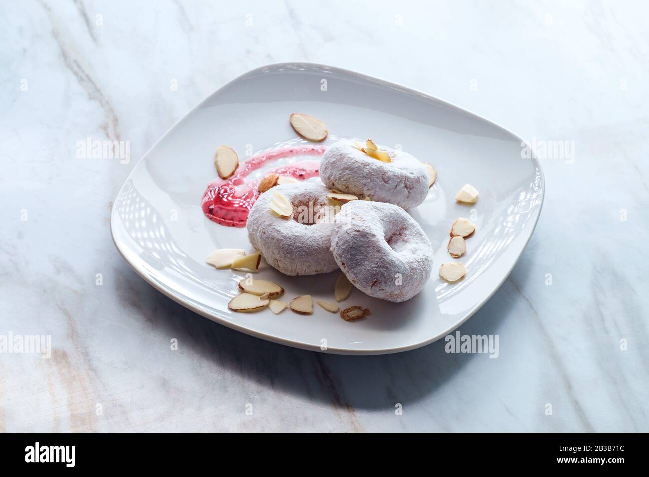 Powdered sugar cake doughnuts with holes served with raspberry jam and slivered almonds Stock Photo