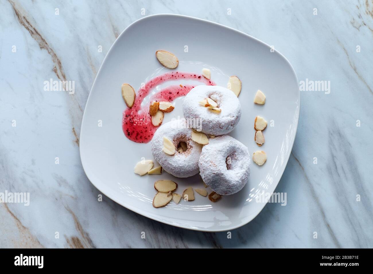 Powdered sugar cake doughnuts with holes served with raspberry jam and slivered almonds Stock Photo