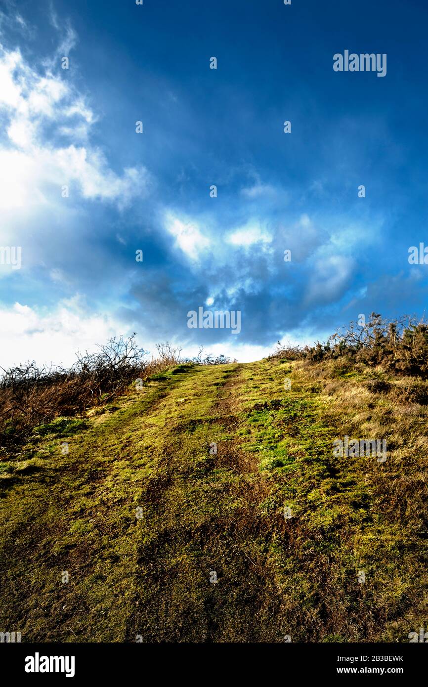 Path going uphill towards blue sky and white clouds ahead, in Aberdeen Golf Club with clouds and grass field. Nigg Bay, Scotland. Stock Photo