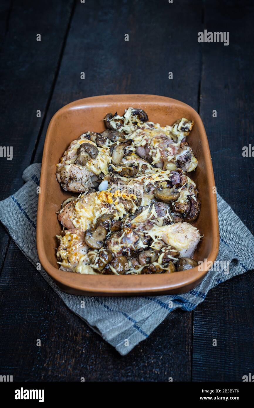 Baked chicken with mushrooms and cheese in a ceramic baking dish on a dark wooden background. In a simple rustic style. Selective flus, blur. Stock Photo