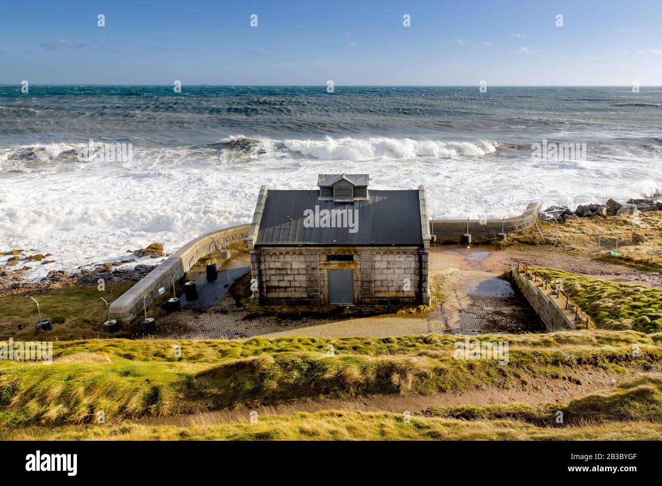 A small building by the sea, below Aberdeen Lighthouse Girdle Ness and its fog horn, rough sea waves Stock Photo