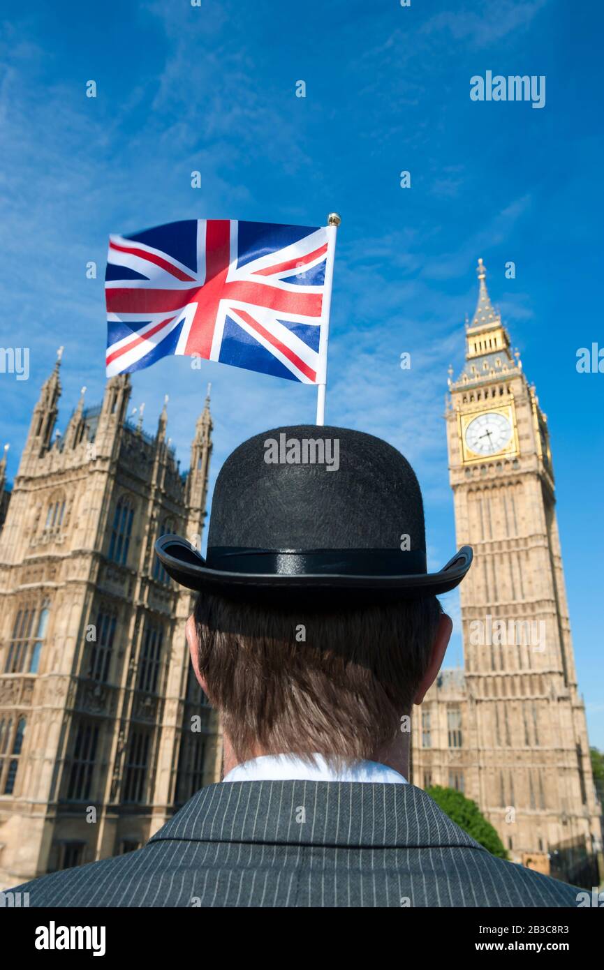 Patriotic British politician wearing a traditional bowler hat with a Union Jack flag standing in front of the Houses of Parliament in London, UK Stock Photo