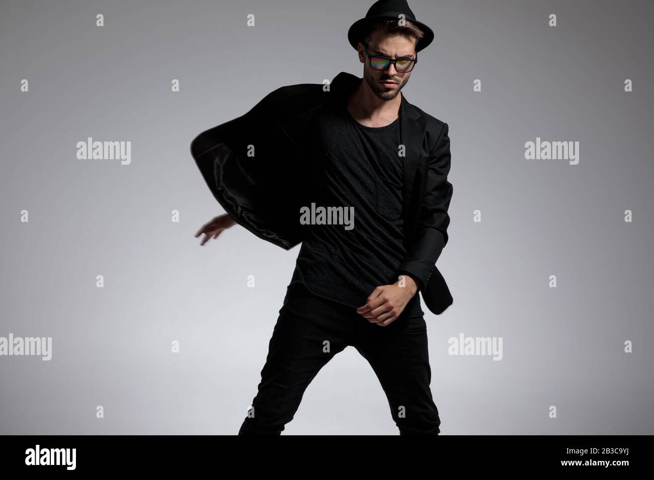 good looking casual man wearing a hat and glasses spinning with a powerful attitude against gray studio background Stock Photo
