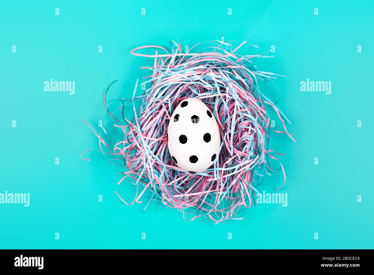 Graphic polka dot hand-painted egg in decorative nest on blue pastel background. Easter concept. Stock Photo