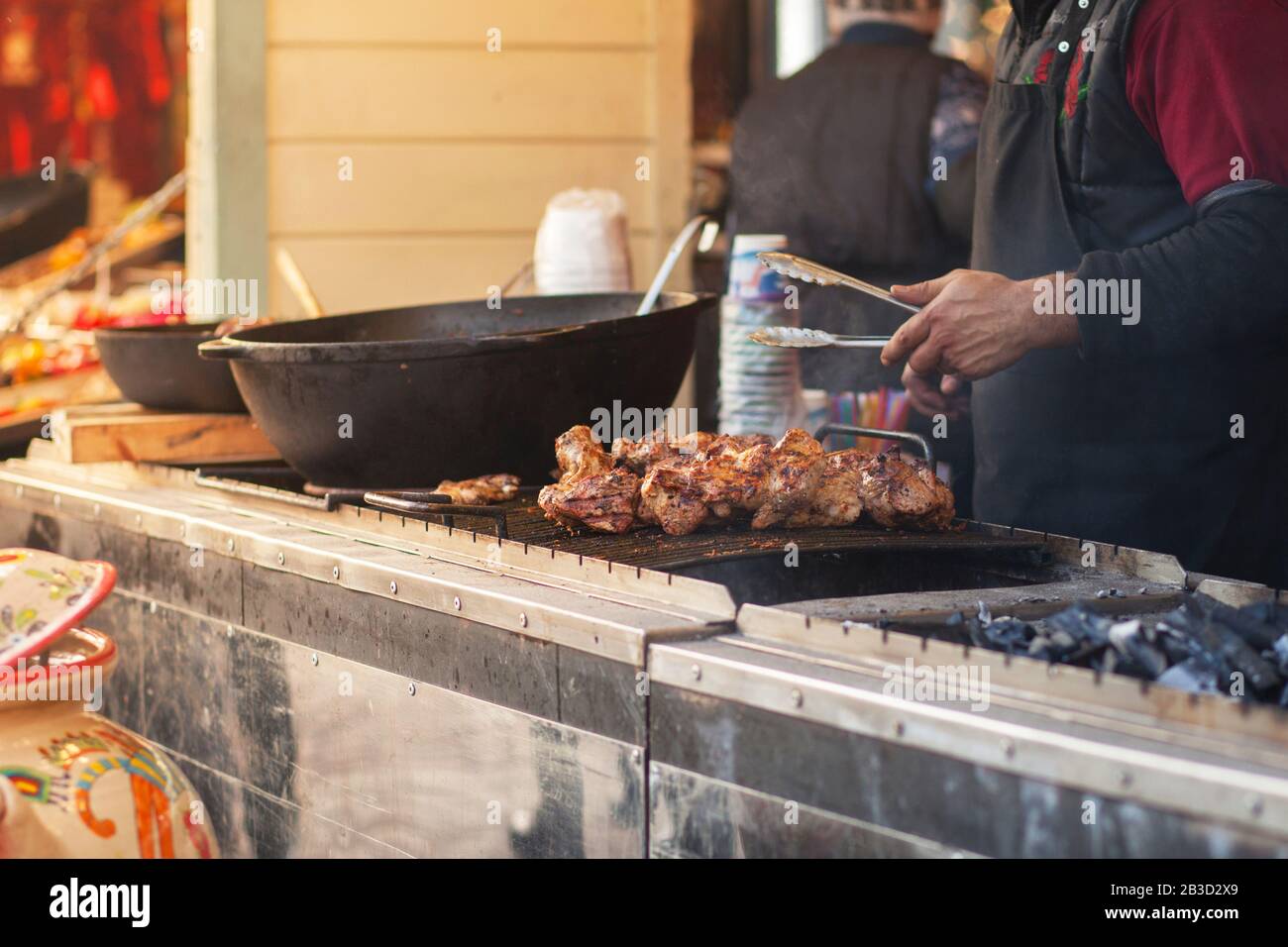 Street food on the grill. Meat on skewers, barbecue. In the background are visible the hands of a man who is cooking kebab. Outside. Horizontal photo. Stock Photo