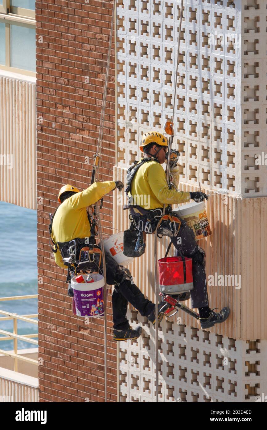 Two men wearing PPE safety gear hanging from ropes in bosuns chair