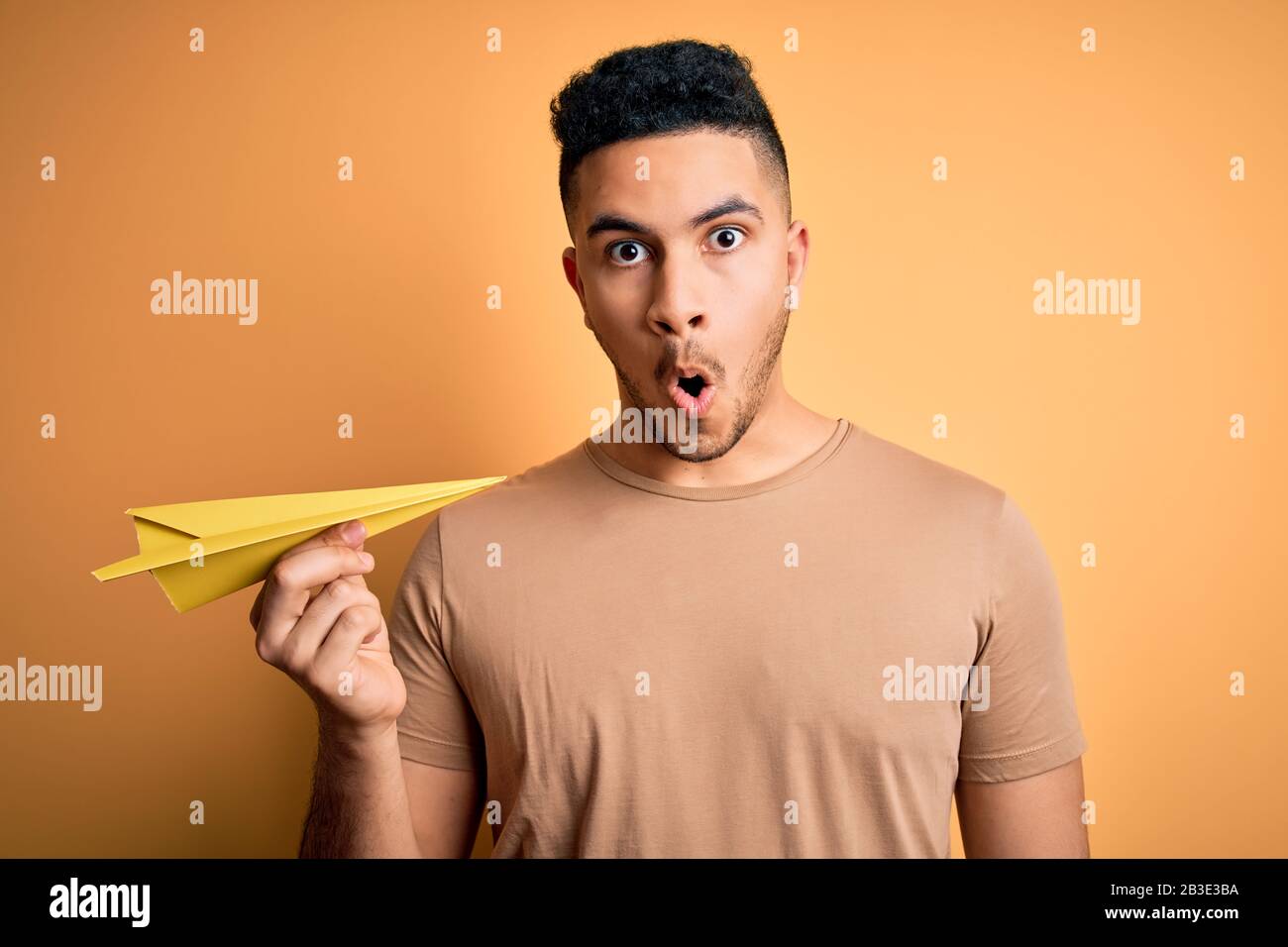 Afraid Paper Young handsome man holding paper airplane over isolated yellow ...