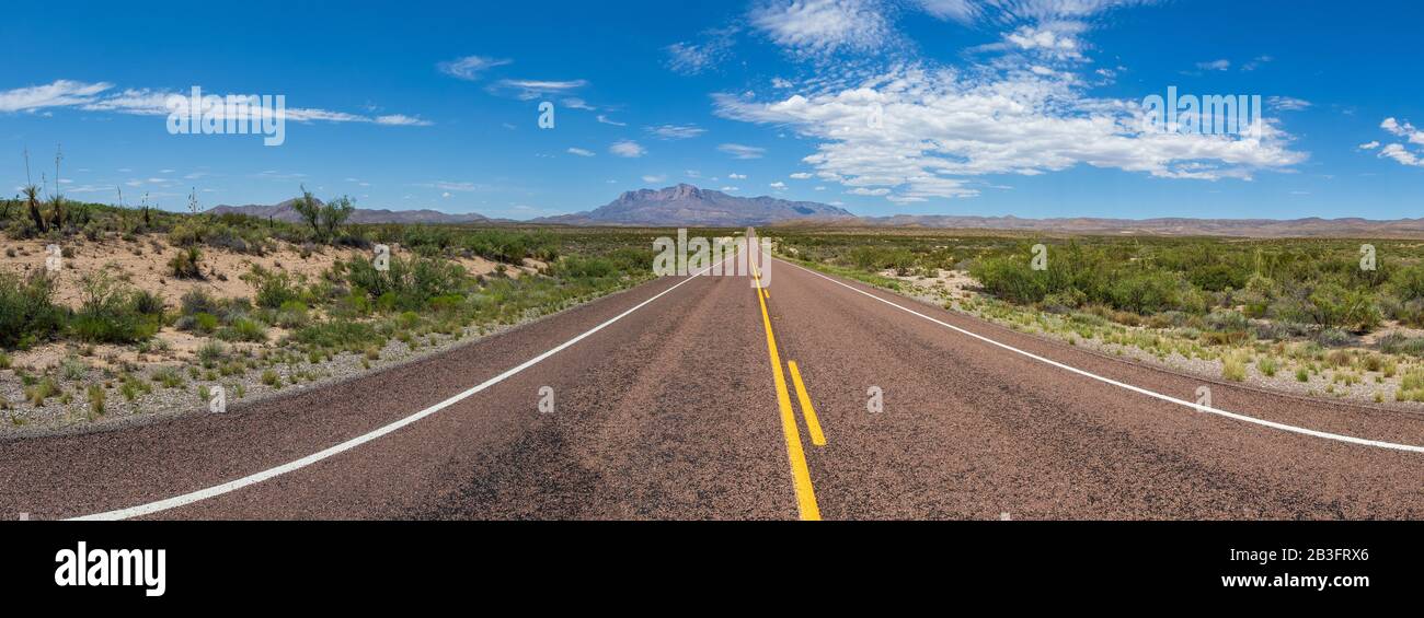 Panoramic view of a long straight road in the desert, leading to a beautiful mountain range under a blue sky with clouds Stock Photo