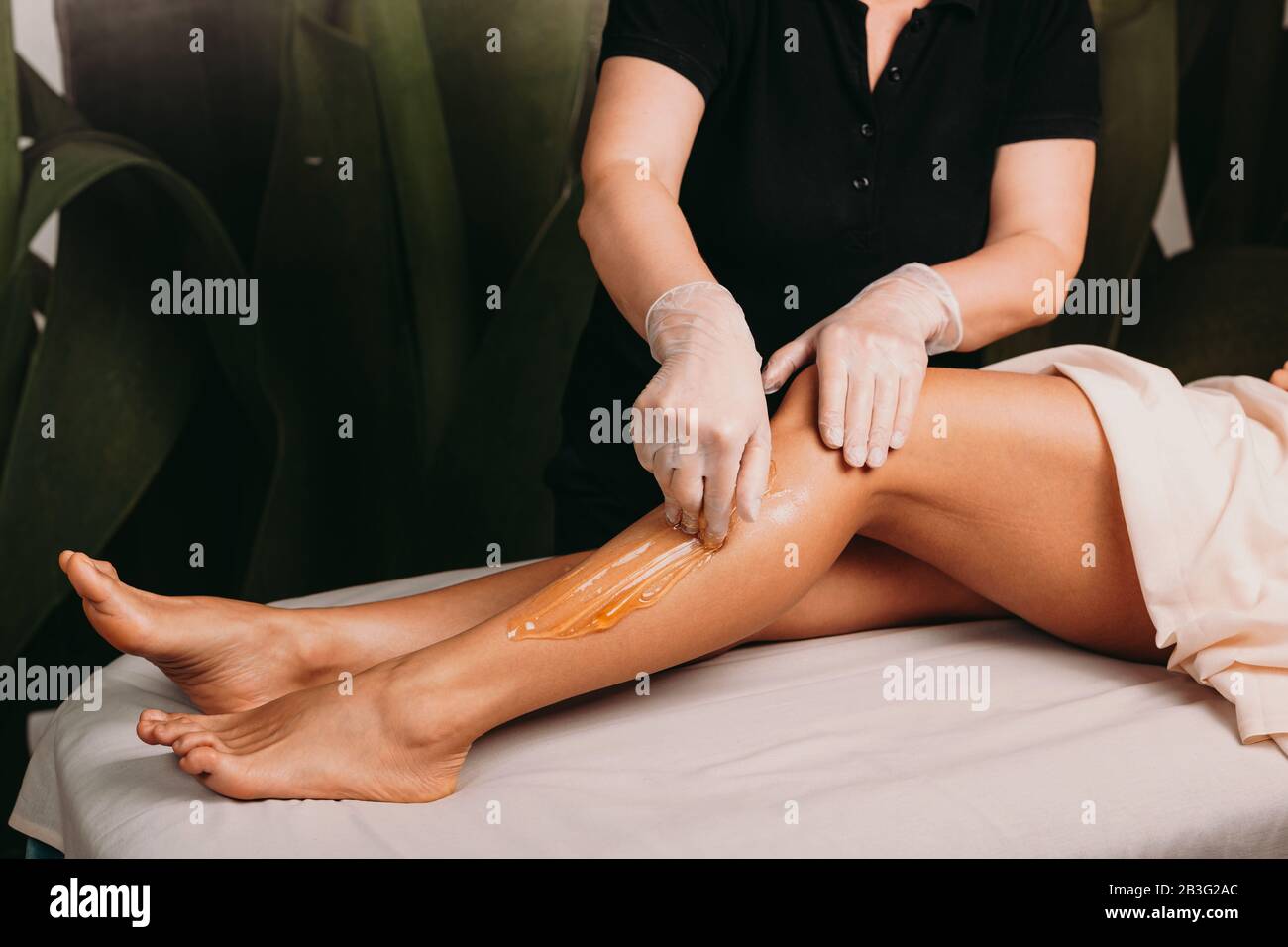 Caucasian lady with beautiful legs is having a sugar epilation during a professional spa procedure Stock Photo